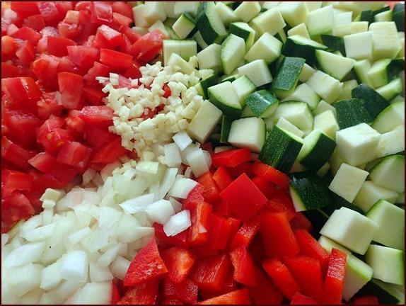 Ingredients for zucchini ratatouille: Tomatoes, red bell peppers, onions, garlic, and zucchini.